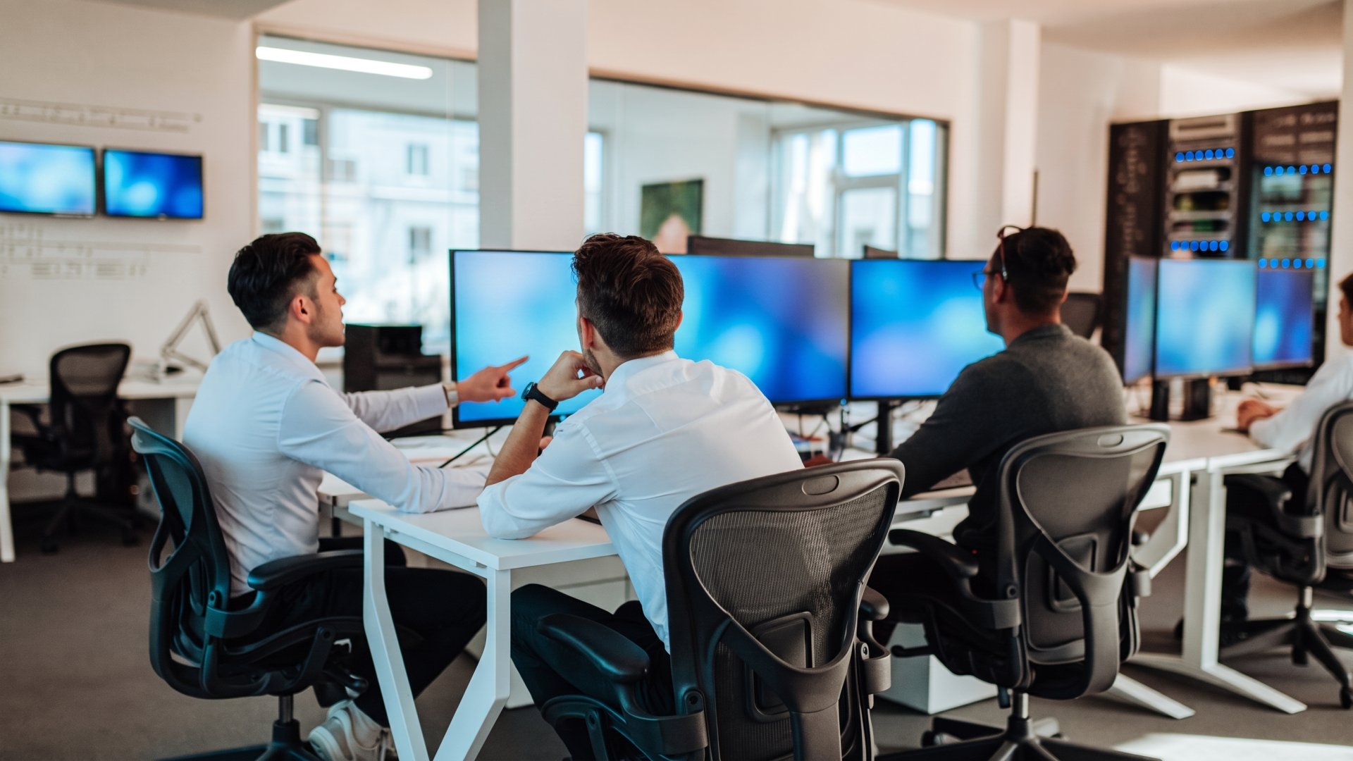 IT-Team von badata arbeitet gemeinsam an Monitoring-Bildschirmen, im Hintergrund Serverschränke